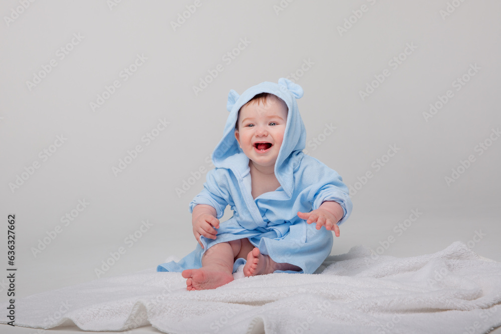 Cute happy laughing baby in a soft bathrobe after bathing plays on a white background. The child is wrapped in a clean and dry towel. Washing, baby hygiene, health and skin care Cute happy laughing baby in a soft bathrobe after bathing plays on a white background. The child is wrapped in a clean and dry towel. Washing, baby hygiene, health and skin care