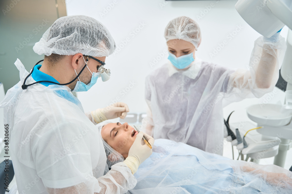 Male dentist treats dental canal to young woman under microscope Male dentist treats dental canal to young woman under microscope