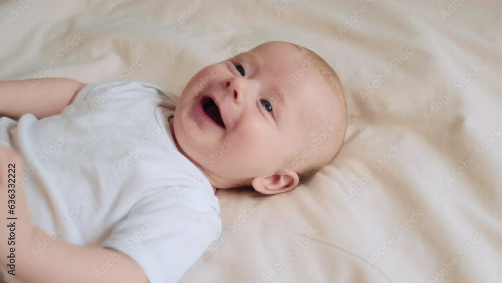 Close up portrait of happy funny cute little newborn boy with smiling face lying on comfortable bed in bedroom at home. Cheerful infant baby resting playing lying down on blanket. Childhood concept Close up portrait of happy funny cute little newborn boy with smiling face lying on comfortable bed in bedroom at home. Cheerful infant baby resting playing lying down on blanket. Childhood concept
