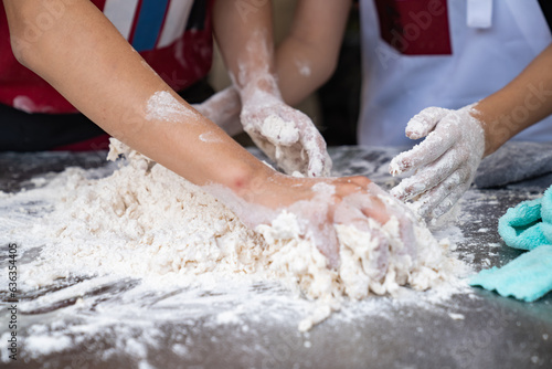 Two skilled Asian men showcase their expertise as they deftly work together, their four hands skillfully kneading and threshing flour on aluminum plate, in preparation for crafting fresh