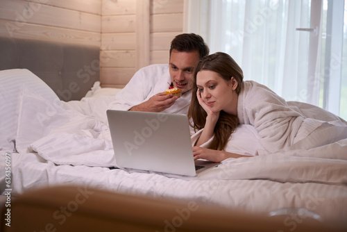 Couple laying in bed and looking on laptop screen