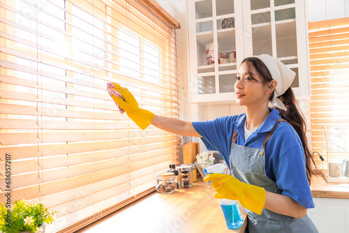 Close-up attractive housekeeper female worker in uniform wipe kitchenware happy disinfect household and kitchen, housewife or employee from cleaning service company wearing gloves and apron multitask