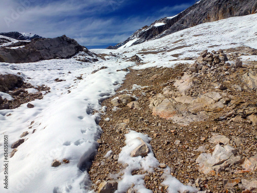 Scattered stone cobblestones on a snowy mountain peak against the background of a blue sky with light clouds