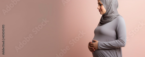 A pregnant woman in a hijab on a plain background in the studio. A beautiful woman with a scarf on her head is waiting for the birth of a child.