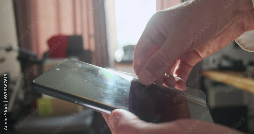 Man rips off an old protective film from smartphone screen. Close-up, side view, light reflection from clear phone black display. Man rips off an old protective film from smartphone screen. Close-up, side view, light reflection from clear phone black display.