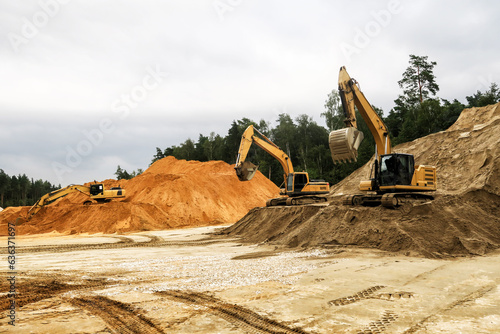 a crawler excavator loads sand into a truck. Large hills and heaps of sand, gravel, crushed stone of yellow, gray and black colors