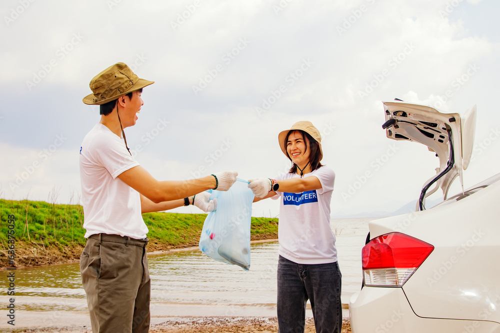 Asian volunteer couple willing to voluntarily collect garbage and clean up in natural tourist attractions by helping to carry garbage into the car to dispose of recyclable waste for the environment. Asian volunteer couple willing to voluntarily collect garbage and clean up in natural tourist attractions by helping to carry garbage into the car to dispose of recyclable waste for the environment.