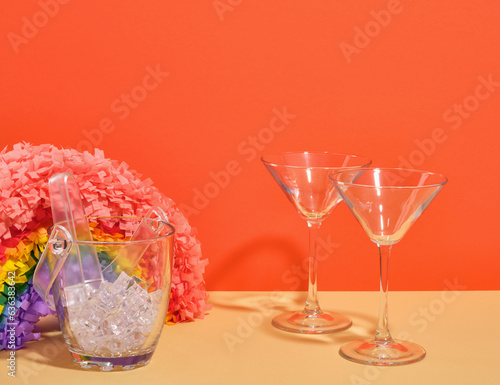 A festive rainbow pinata, glass ice bucket and two glasses for alcoholic drinks. Concept of birthday party.