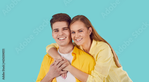 Studio shot of happy family looking at camera and smiling. Young married couple in yellow shirts isolated on turquoise background. Young man with his girlfriend. Pretty woman hugging her boyfriend © Studio Romantic