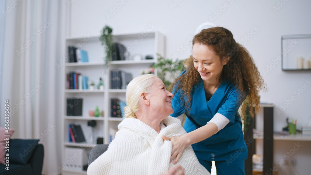 Caring nurse bringing blanket to warm up senior woman in a retirement home Caring nurse bringing blanket to warm up senior woman in a retirement home