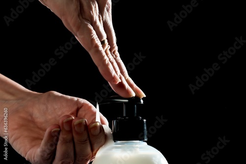 Closeup of the hands of a person putting hand cream on one hand on the black background photo