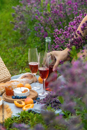 Wicker basket with delicious food for a romantic picnic in a lavender field, wine, fruits, berries.