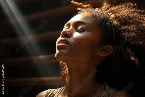 A thought provoking portrait of a young African woman in her late twenties her eyes closed in reflection. The sun falls on her skin