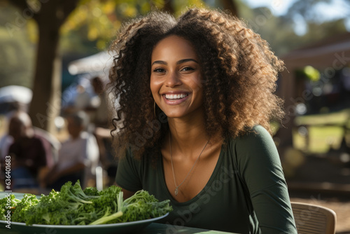 A Black woman in a green tunic sitting on a bench in a park and eating a healthy snack with a satisfied expression.