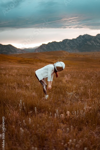 Woman in a white helmet standing in a field with mountains in the backdrop. photo