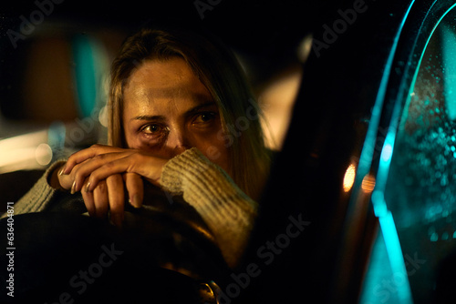 A young Caucasian woman, marked by the harrowing evidence of domestic abuse with distinct bruises and darkened eyes, sits in her car, leaning heavily on the steering wheel. photo
