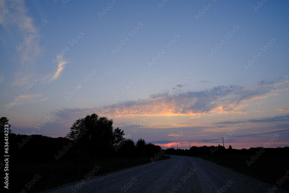 beautiful colorful Latvia country road landscape with trees, blue sky and colorful clouds in summer sunset light