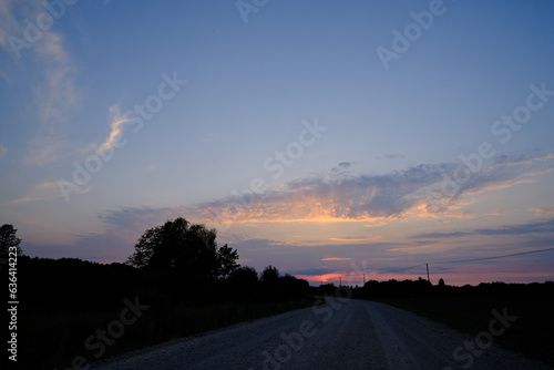beautiful colorful Latvia country road landscape with trees  blue sky and colorful clouds in summer sunset light
