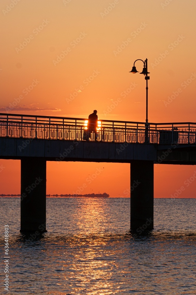 Low-angle of a boardwalk with a seascape view at sunset and a man silhouette walking there