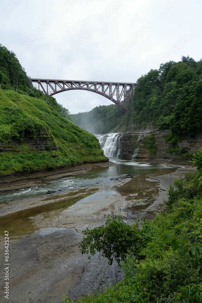 Scenic view of a bridge crossing a waterfall with a lush green forest in Letchworth State Park Scenic view of a bridge crossing a waterfall with a lush green forest in Letchworth State Park
