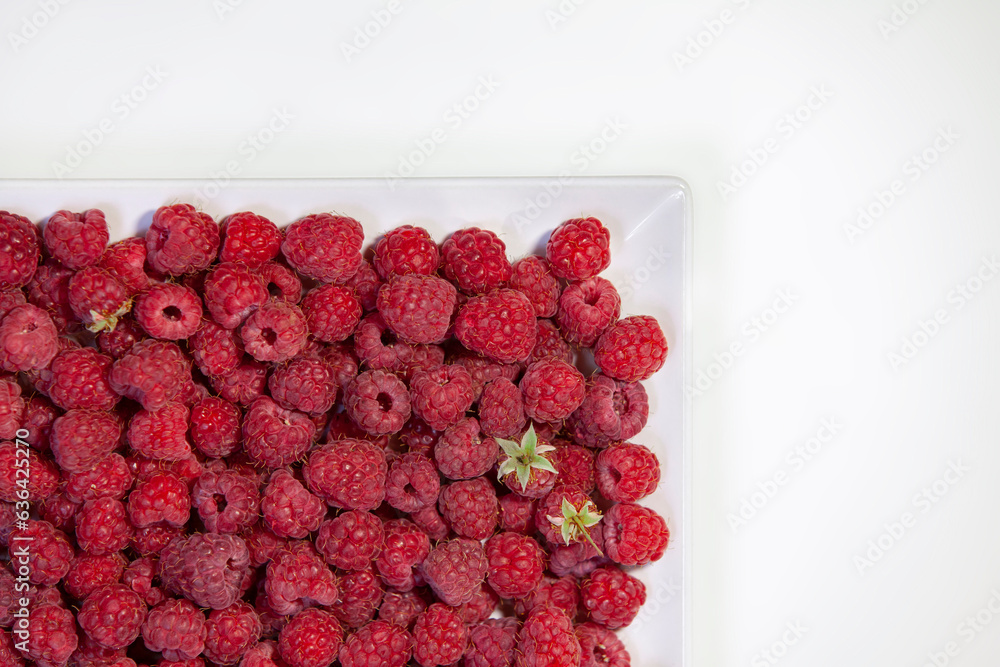 Fresh ripe raspberries on a square plate on a white background. Berries with a huge amount of vitamins. Top view. Copy space.