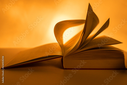 In backlighting, the pages of a large book are turned up close to the front to emphasise the sinuous movement of the pages. Intense bokeh. Warm atmosphere. Copy space.