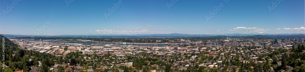 Panoramic view of a large city surrounded by lush forest and towering mountains in the background