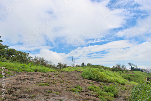 Panoramic landscape view of beautiful lush green scenery of Sinhagad fort with bright blue sky and huge white clouds in Pune, Maharashtra, India