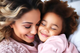 Mixed race mother and daughter in pink clothes lie in bed and hug.