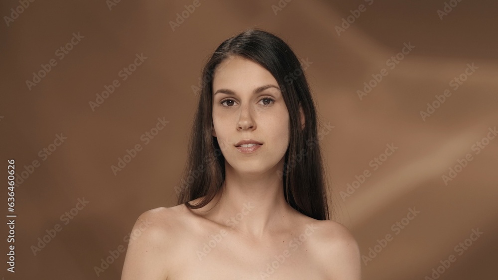 Obraz premium Portrait of a young longhaired seminude woman in the studio on a brown background. The concept of beauty, cosmetology, care and women's health.