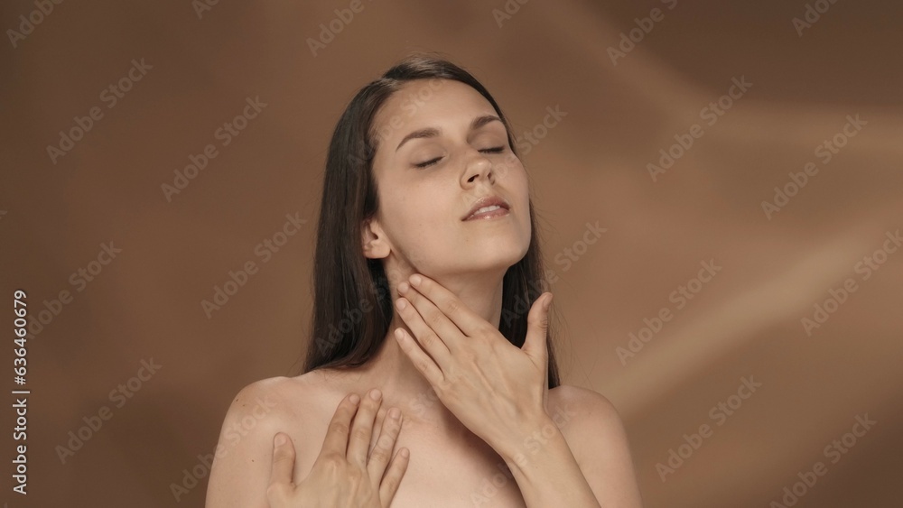 The young woman enjoys her smooth, clean silky skin, touches the neck and chest. Portrait of a seminude smiling woman in the studio on a brown background. The concept of beauty, cosmetology, skin care The young woman enjoys her smooth, clean silky skin, touches the neck and chest. Portrait of a seminude smiling woman in the studio on a brown background. The concept of beauty, cosmetology, skin care