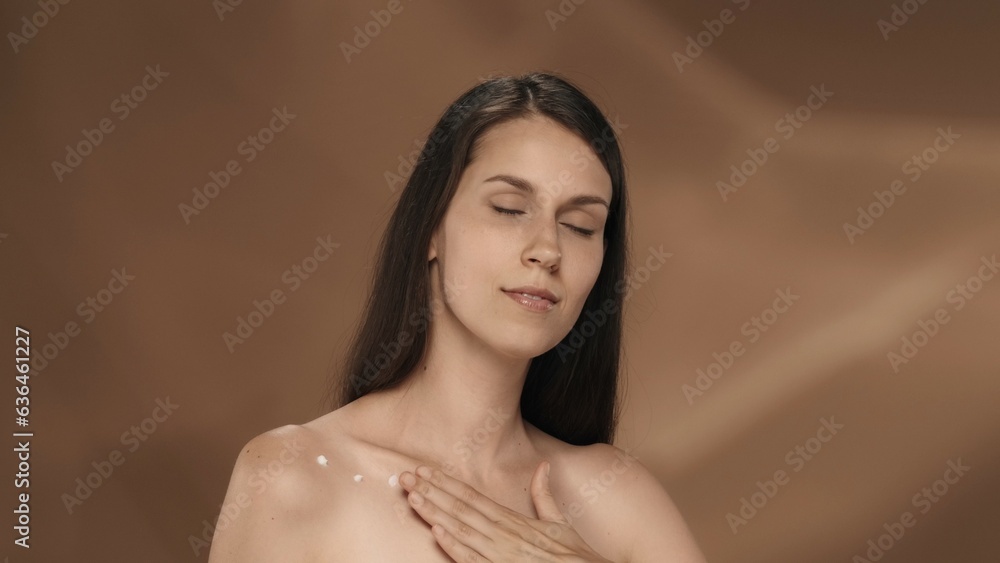 The young woman enjoys her smooth, clean silky skin, touches chest thorax. Portrait of a seminude woman in the studio on a brown background. The concept of beauty, cosmetology, skin care. The young woman enjoys her smooth, clean silky skin, touches chest thorax. Portrait of a seminude woman in the studio on a brown background. The concept of beauty, cosmetology, skin care.