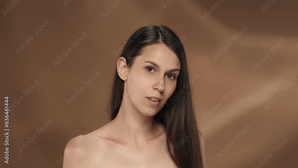 Portrait of a young longhaired seminude woman in the studio on a brown background. The concept of beauty, cosmetology, care and women's health. Portrait of a young longhaired seminude woman in the studio on a brown background. The concept of beauty, cosmetology, care and women's health.