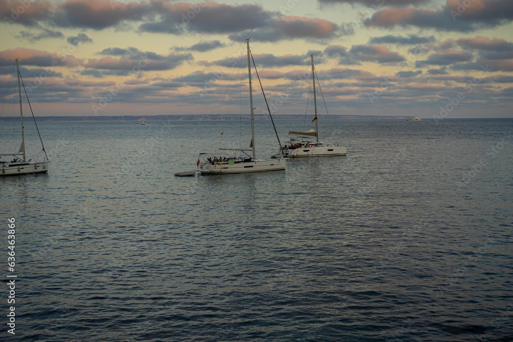 Recreational boats lie anchored in a Mallorca cove, basking in the amber embrace of sunset, capturing the essence of Balearic tranquility. Recreational boats lie anchored in a Mallorca cove, basking in the amber embrace of sunset, capturing the essence of Balearic tranquility.