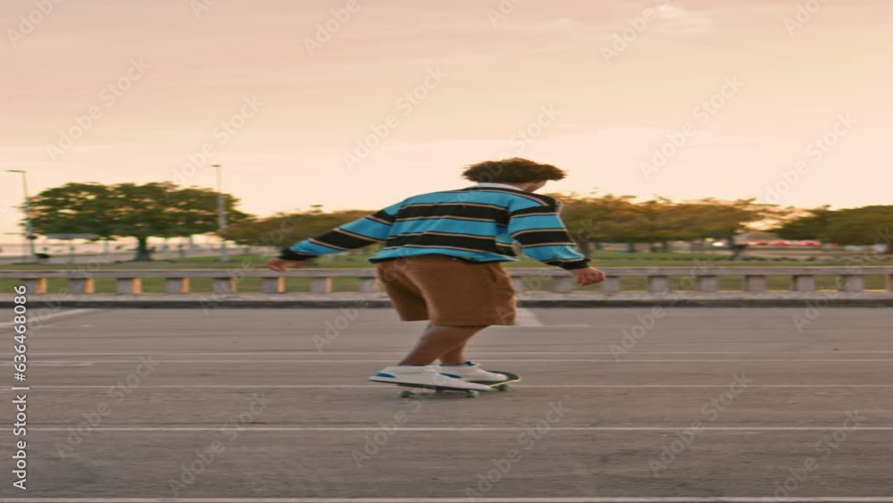 Young man balancing skateboard at evening back view. Guy riding skate vertically