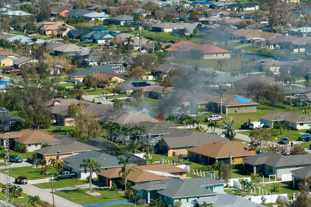 View from above of burning private house on fire and firefighters extinguishing flames after short circuit caused to ignite roof damaged by hurricane Ian wind. Home disaster in Florida suburban area