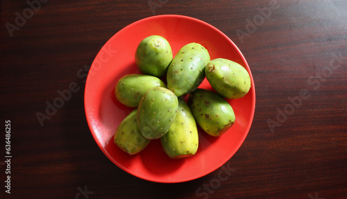 Obraz na plátně Plato rojo con tunas verdes sobre superficie de madera cafe.