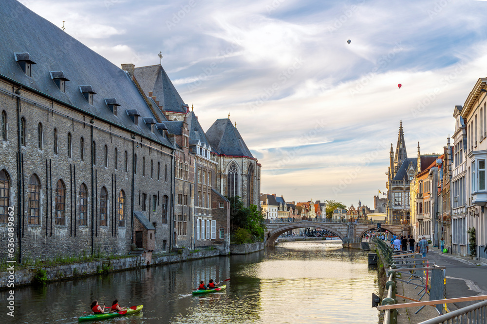 Two groups of kayakers boat the Leie River through the historic medieval old town of Ghent, Belgium, at twilight.