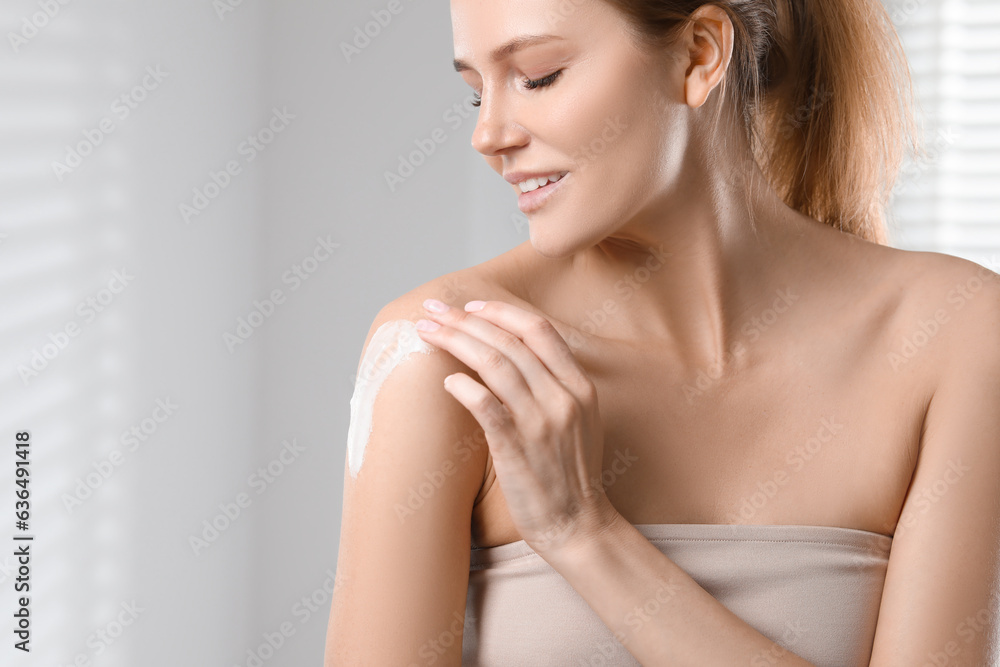 Beautiful woman applying body cream onto shoulder indoors, space for text Beautiful woman applying body cream onto shoulder indoors, space for text