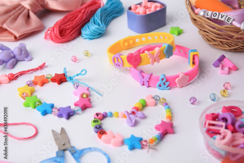 Kid's handmade beaded jewelry and different supplies on white background, closeup