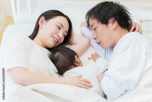 ベッドで赤ちゃんと添い寝する夫婦