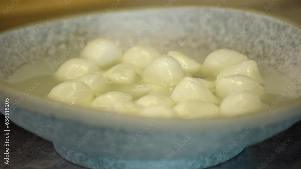 Balls of mozzarella cheese. A hand puts a plate of cheese on the table. Balls of mozzarella cheese. A hand puts a plate of cheese on the table.