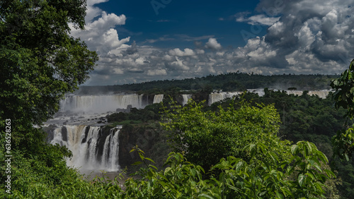 Waterfall landscape. Streams of water cascade from the ledges. Lush tropical vegetation all around. Clouds in the blue sky. Iguazu Falls. Brazil.