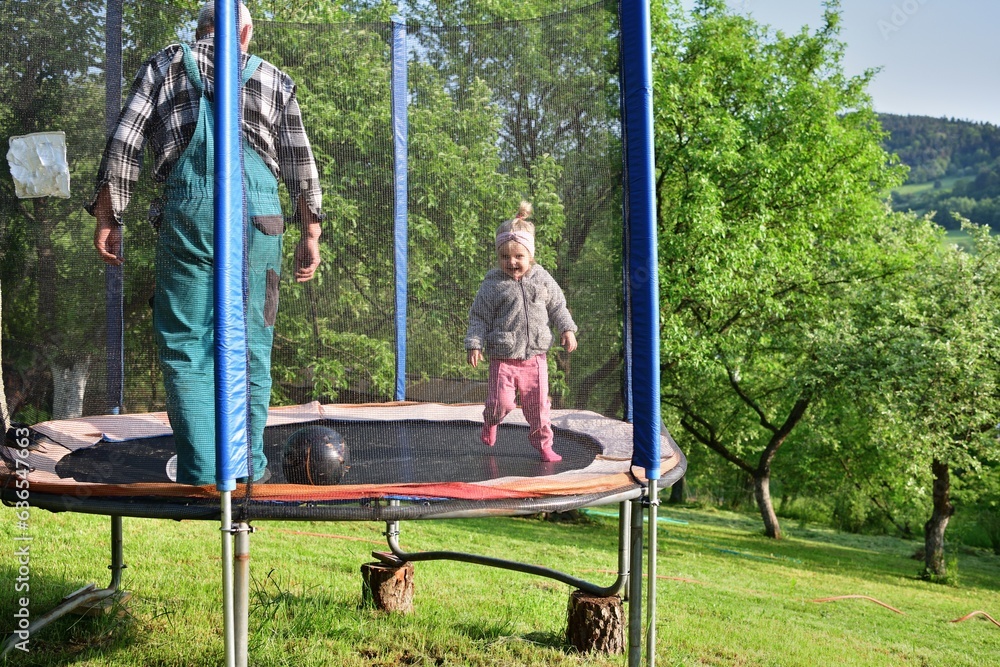 A 2-year-old girl jumps and kicks a ball on a trampoline in the summer