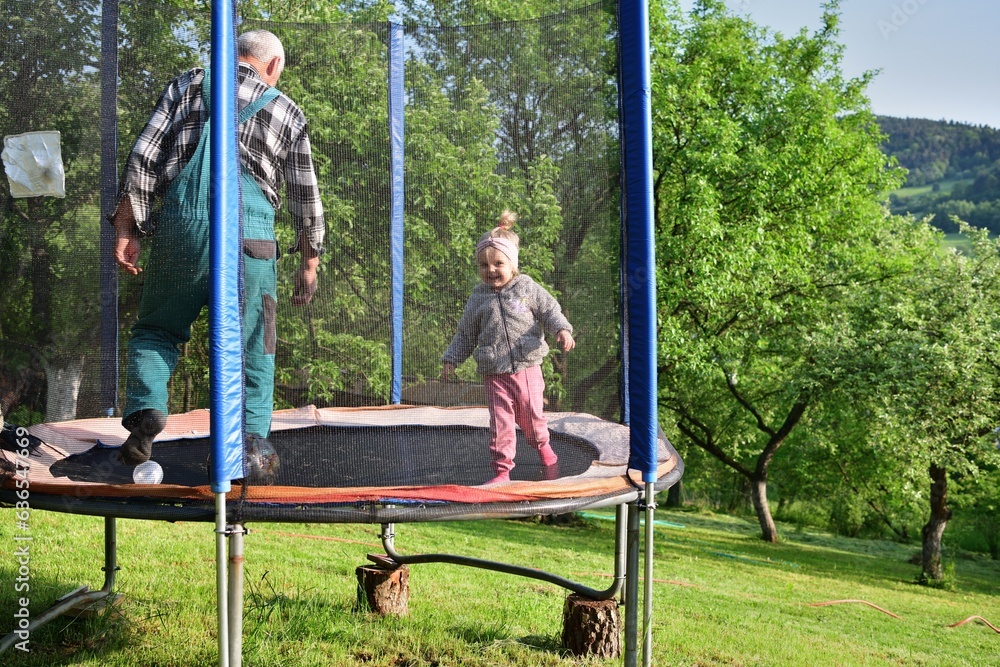 A 2-year-old girl jumps and kicks a ball on a trampoline in the summer
