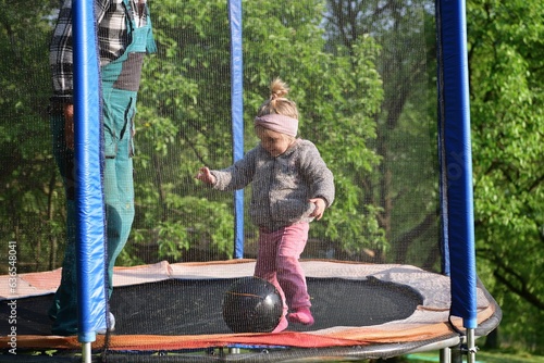 Obraz na płótnie A 2-year-old girl jumps and kicks a ball on a trampoline in the summer w salonie