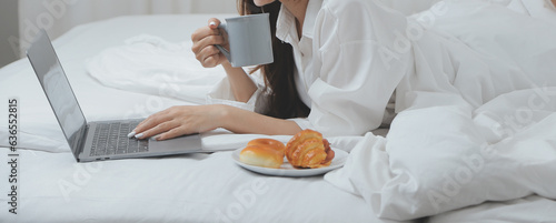 Happy young female in casual clothes smiling and looking at camera while using laptop on bed in bedroom at home