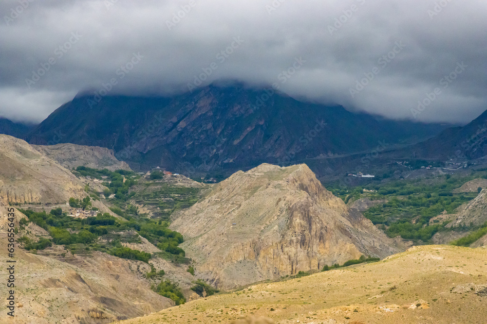 Dark Dramatic Desert Landscape with Foggy Mountains and Distant Houses in Muktinath, Mustang, Nepal