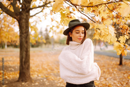 Beautiful woman in stylish clothes and a hat walking in the autumn park at a sunny sunset. The concept of fashion, style.
