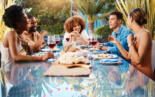 Friends, food and outdoor table for holiday, Christmas or thanksgiving lunch and wine at backyard patio. Young people or social group with alcohol, brunch and drink or talking of summer vacation